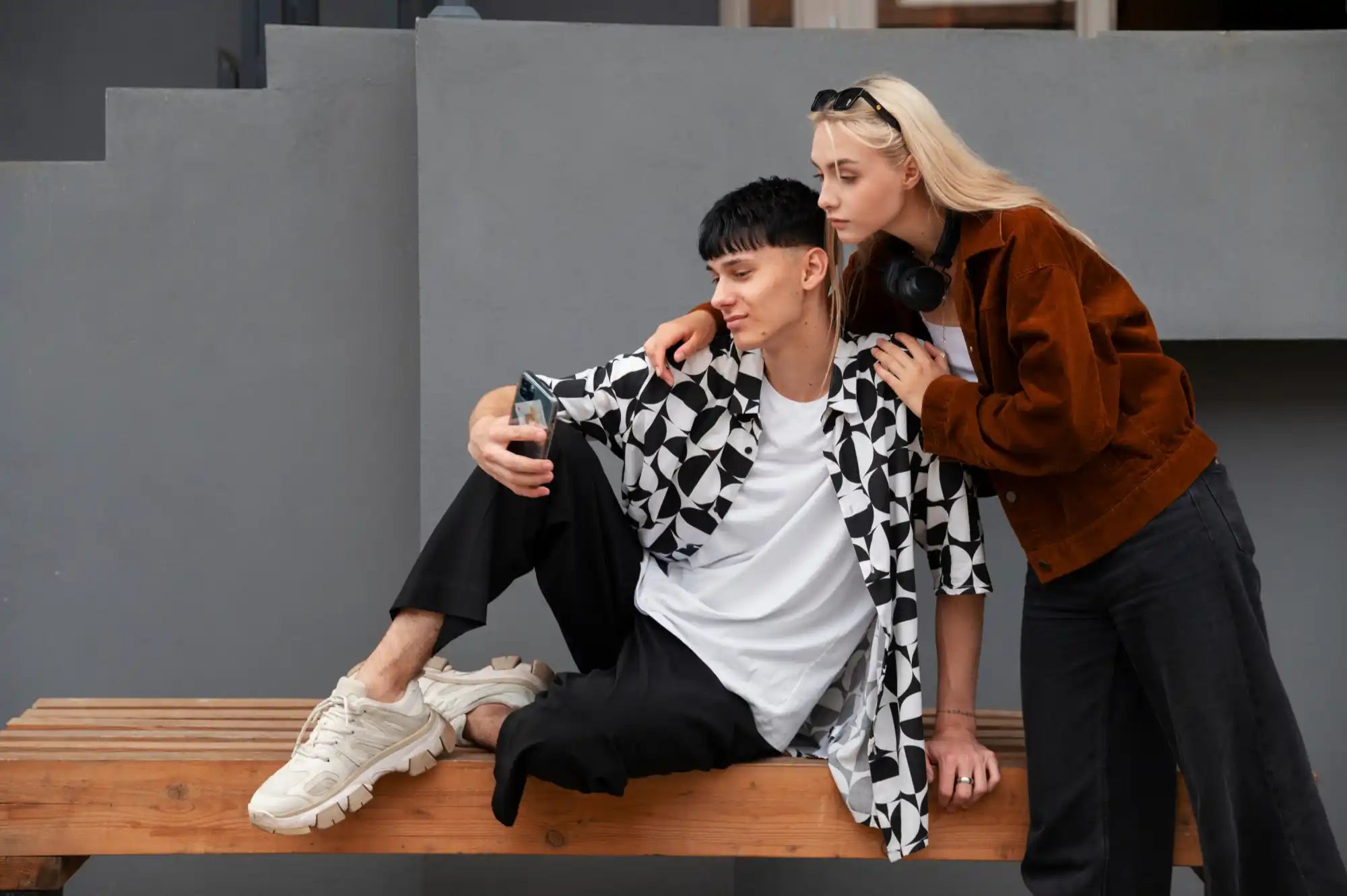 Two people posing casually on a wooden bench while taking a selfie.